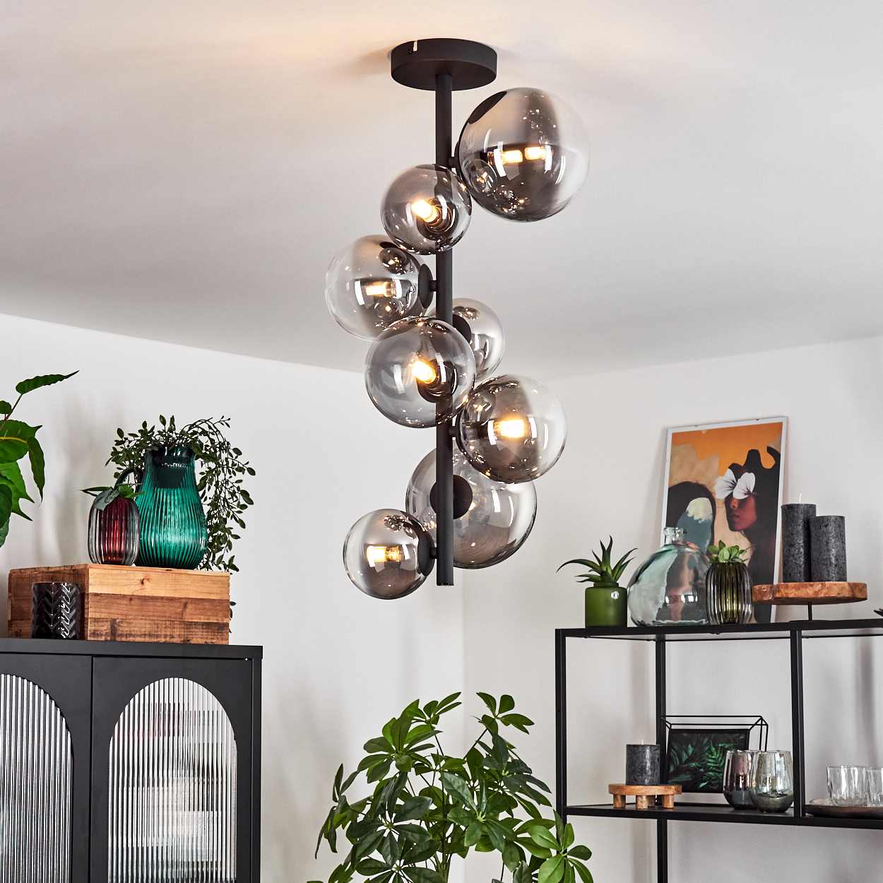 Ein moderner Kronleuchter mit Glaskugeln hängt über einem Raum mit Pflanzen, Regalen und Dekoration. Der Kronleuchter hat Lichter in jeder Kugel.