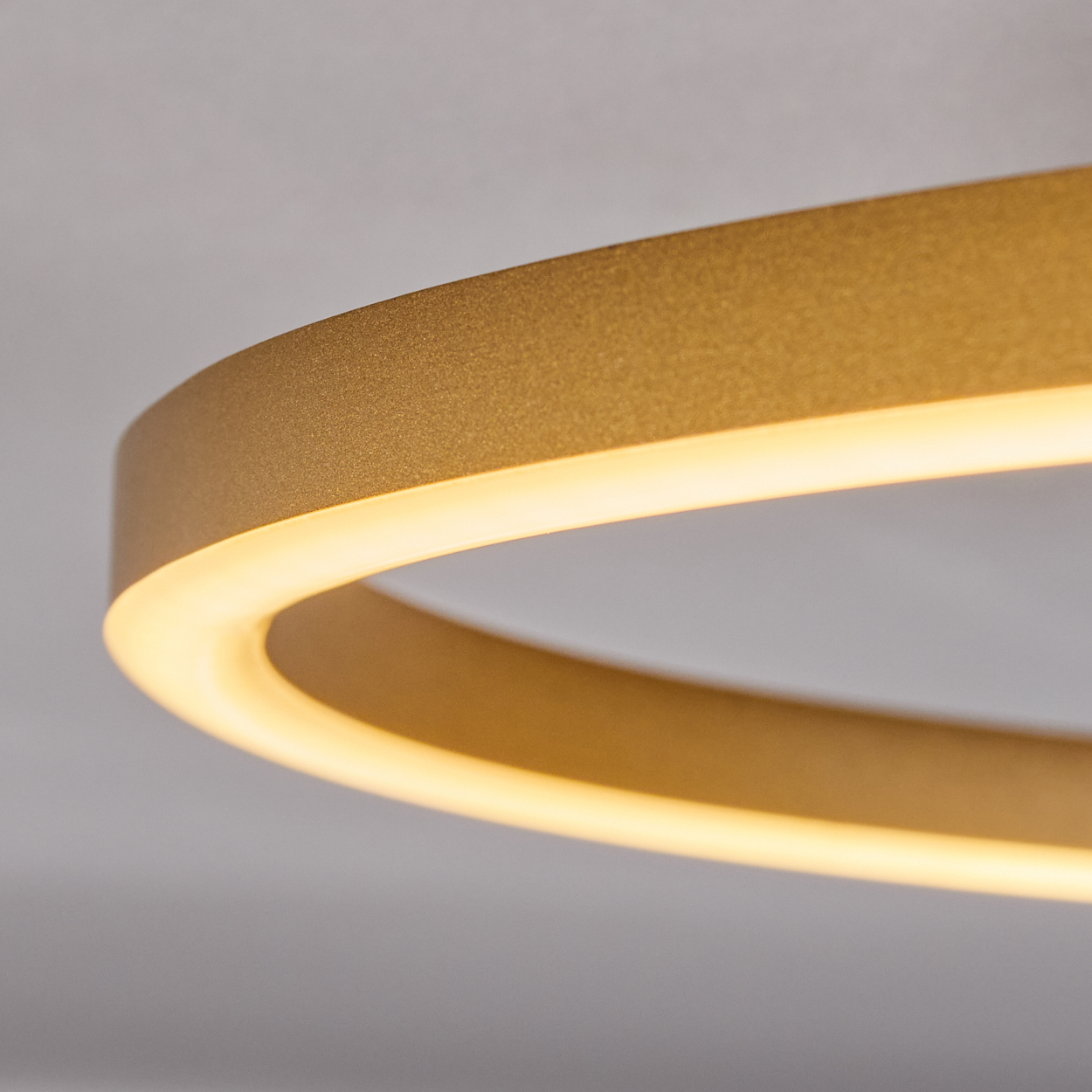 Nahaufnahme einer goldenen, kreisförmigen Leuchte vor weißem Hintergrund. Das Licht strahlt warm.