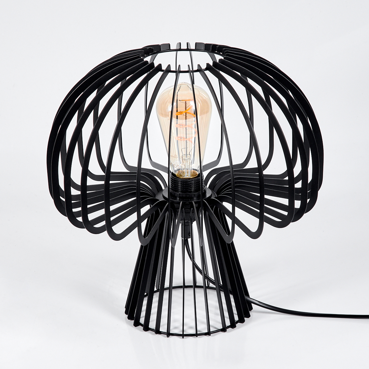 Eine schwarze, käfigartige Lampe mit einer Glühbirne im Inneren steht auf einer weißen Oberfläche. Die Lampe hat ein einzigartiges, künstlerisches Design.