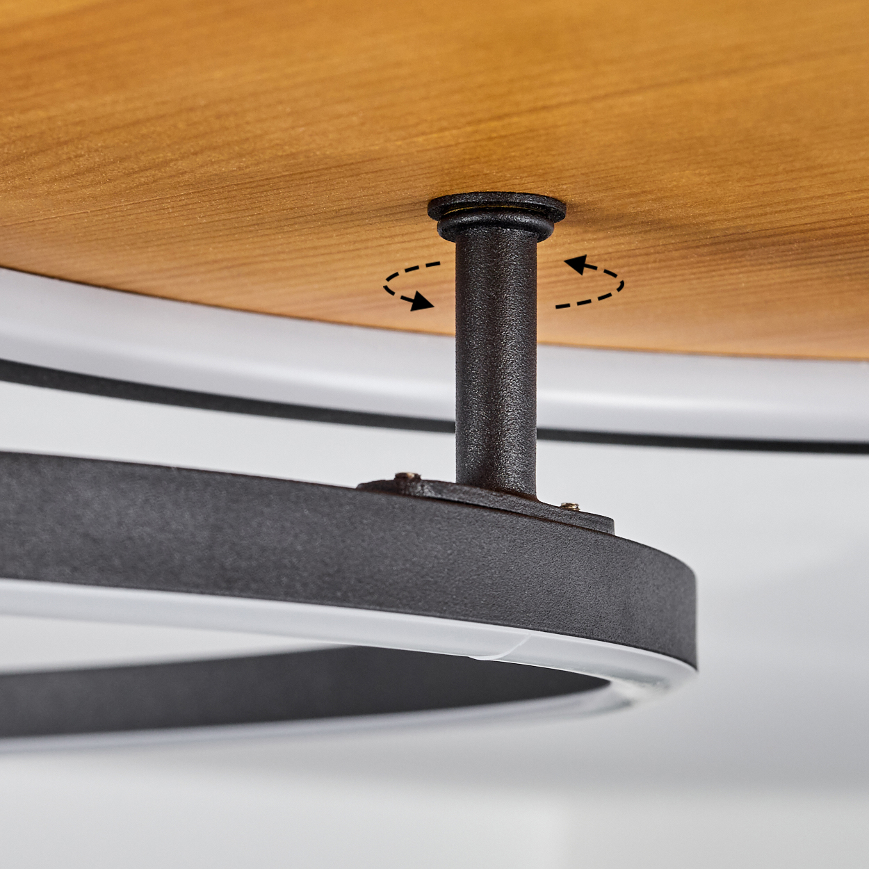 Nahaufnahme eines runden Holztisches und einer schwarzen Metallstütze. Pfeile zeigen die Drehung an. Weißes Neonlicht unter dem Tisch.
