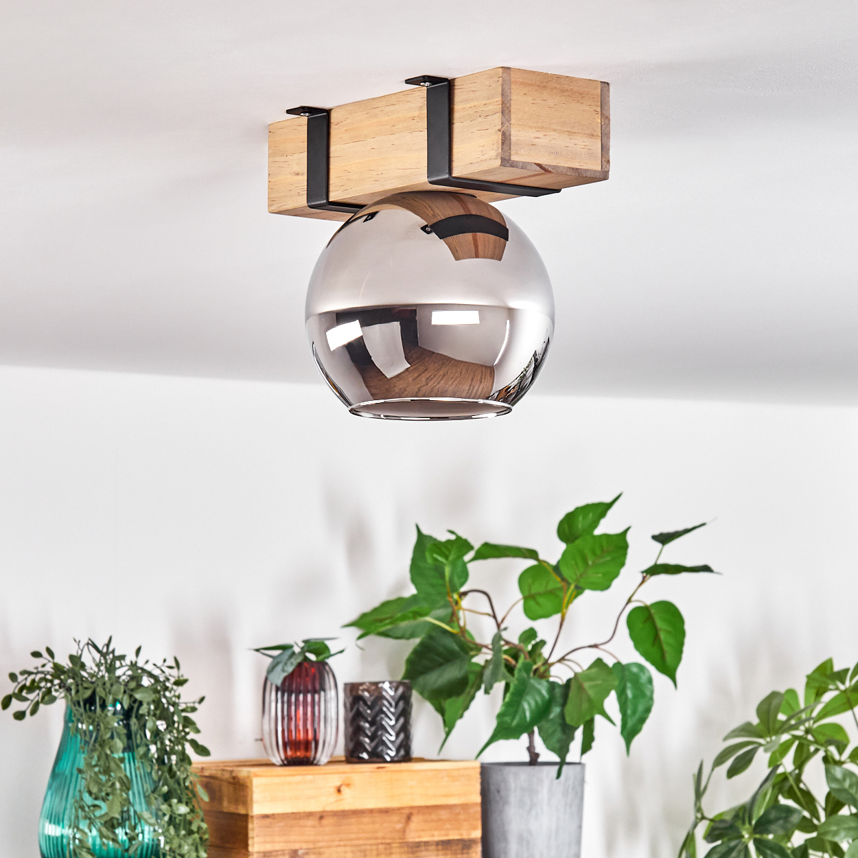 Eine Deckenleuchte mit Holzbalken und reflektierender Kugel. Pflanzen und Vasen unter der Leuchte auf einer Holzoberfläche.