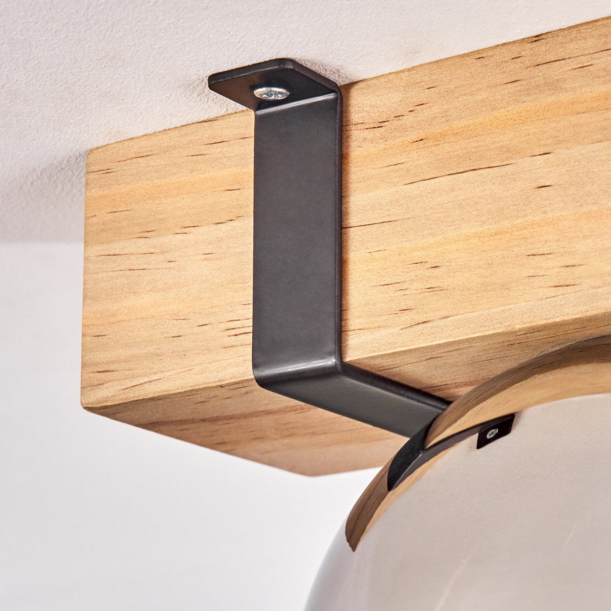 Ein Holzbalken wird von einer schwarzen Metallhalterung gehalten. Der Balken ist an einer weißen Decke befestigt.