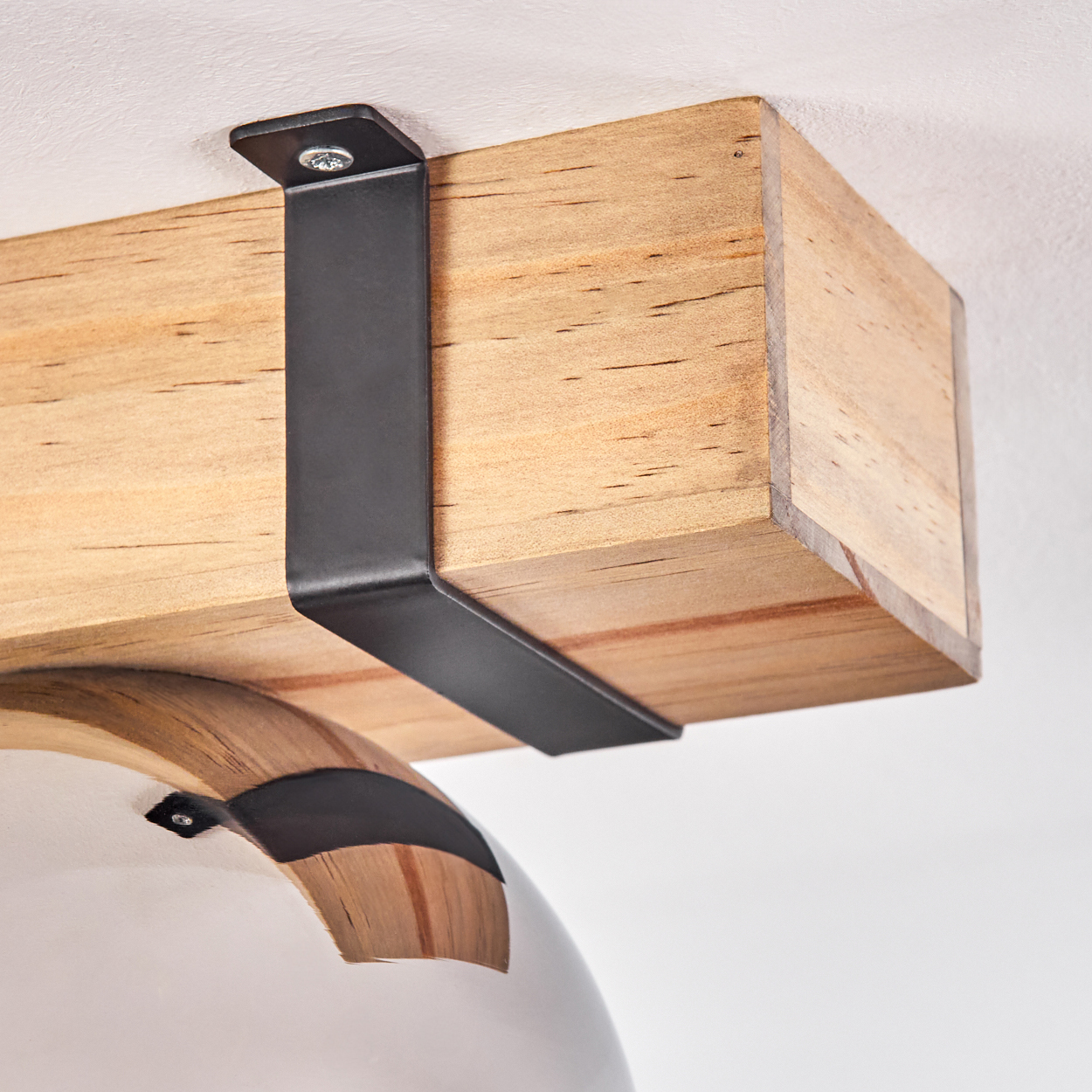 Ein Holzbalken wird von einer schwarzen Metallhalterung gehalten. Darunter befindet sich ein weißes, gebogenes Objekt mit einem dunklen Band.