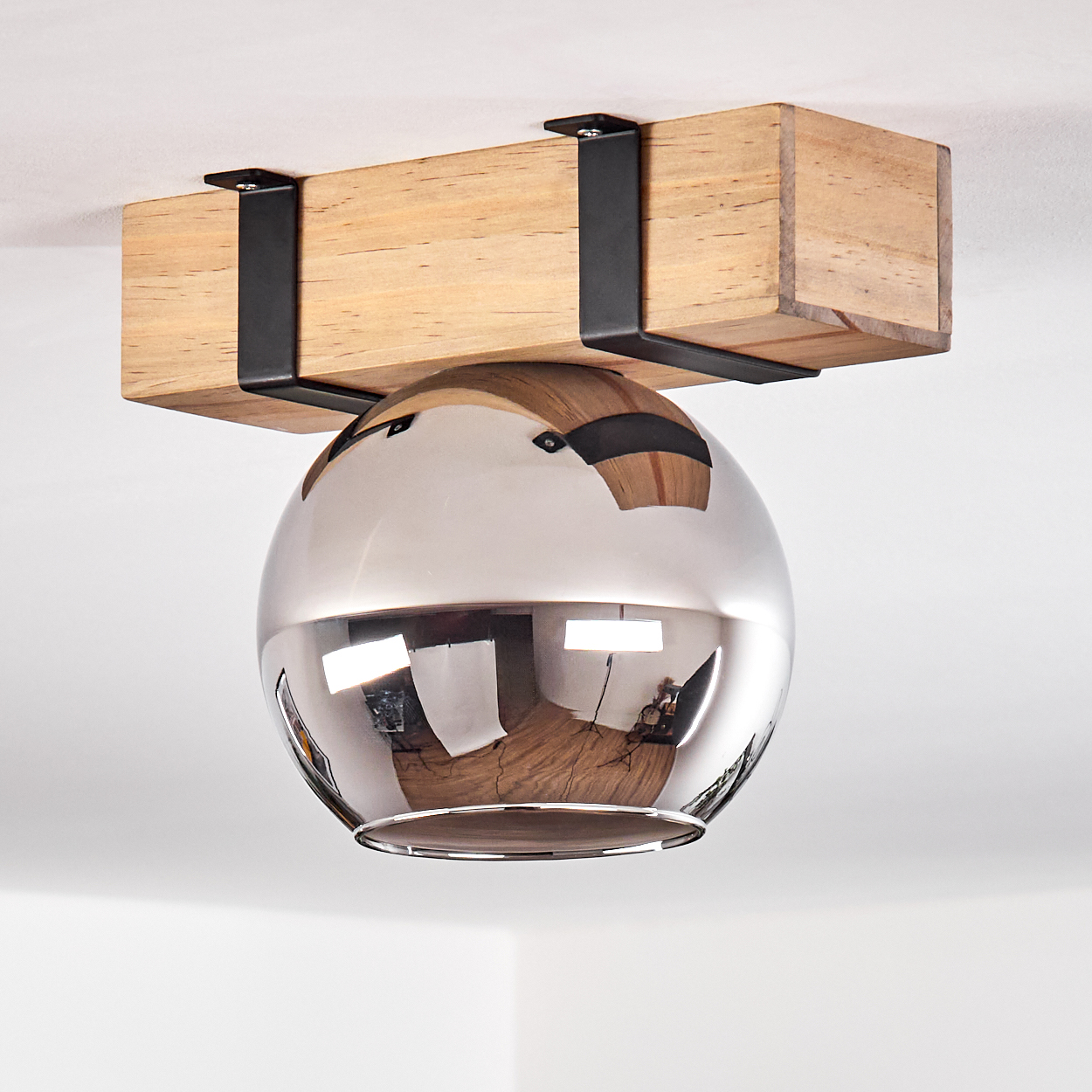 Eine Deckenleuchte mit Holzbalken und einem reflektierenden, kugelförmigen Schirm. Schwarze Metallhalterungen sichern die Leuchte.