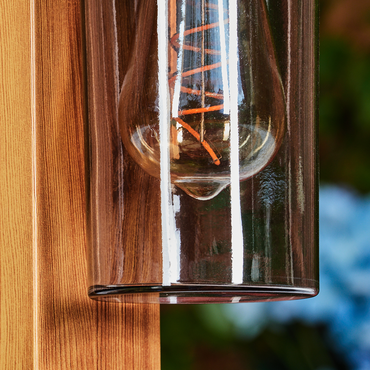 Nahaufnahme einer Glühbirne in Glas. Die Glühbirne hat einen orangefarbenen Glühfaden. Holzpaneele sind links und dahinter.