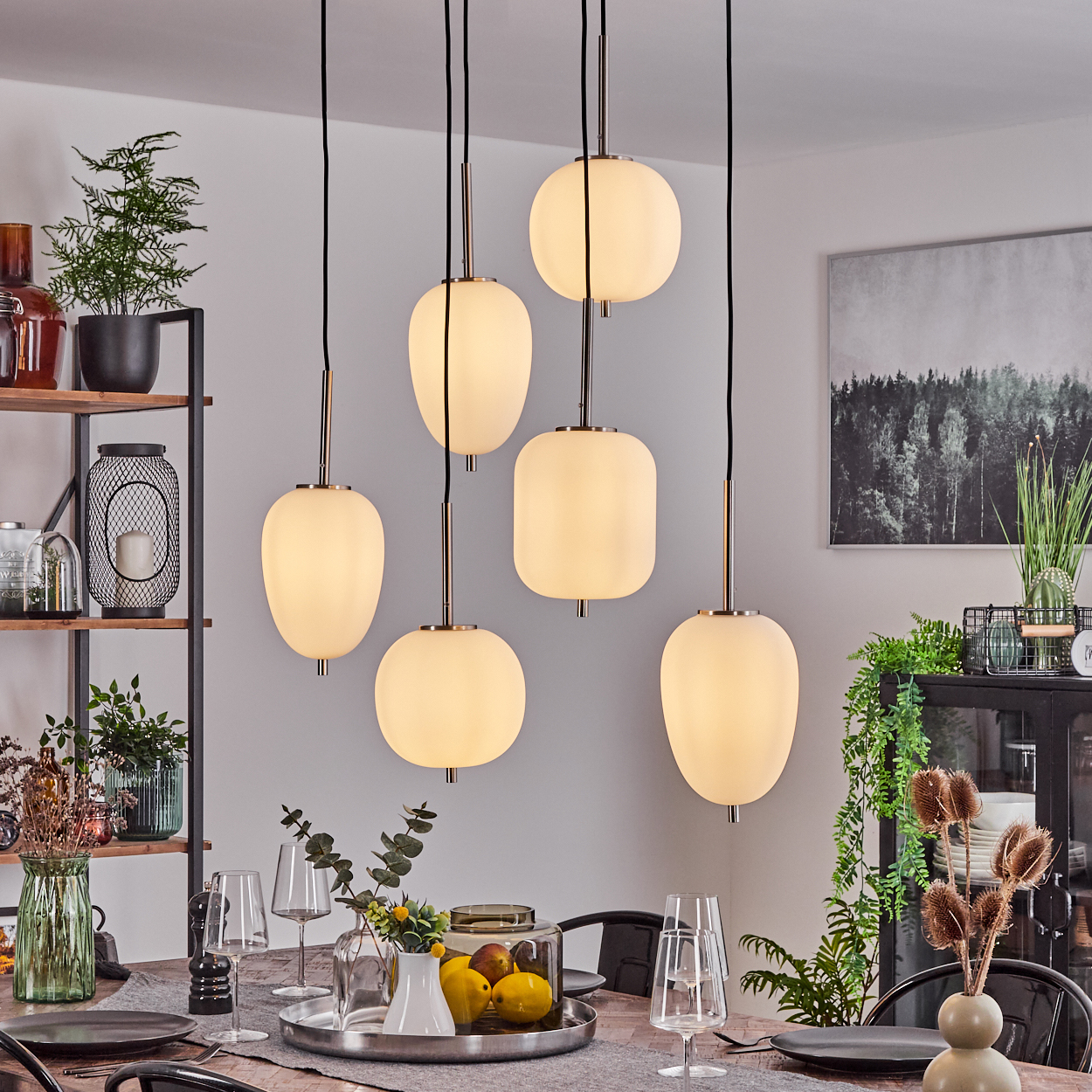 Esszimmer mit Hängelampen, Tischdeko, Zierpflanzen und einem Gemälde an der Wand. Fokus auf Lampen und Tisch.