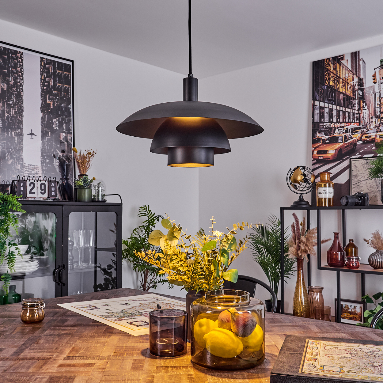 Esszimmer mit Holztisch, schwarzer, mehrstufiger Leuchte und Dekorationen wie Karte, Pflanzen und Glas mit Zitronen.