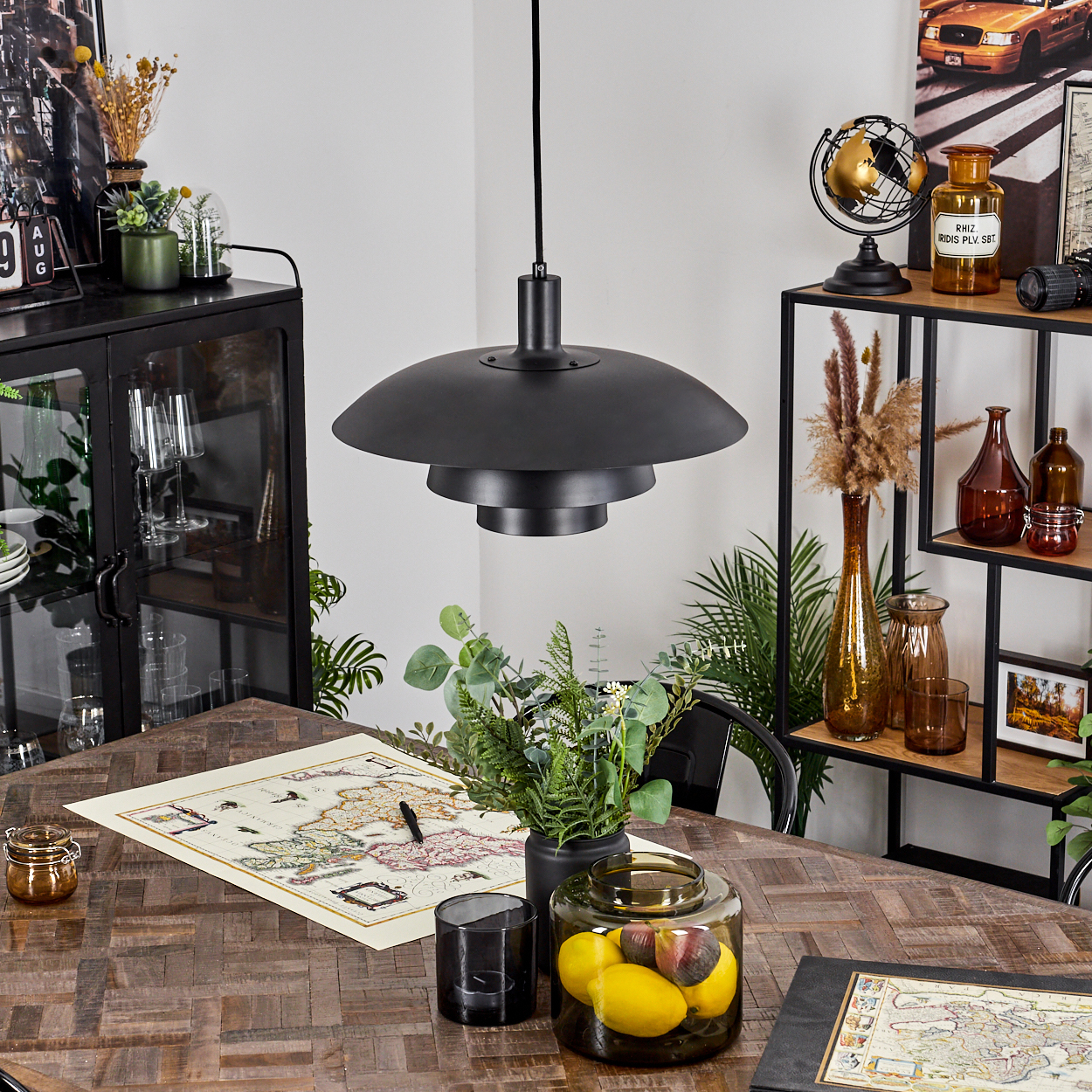 Ein Raum mit Holztisch und Deko. Eine schwarze Lampe hängt darüber. Regale und ein Schrank im Hintergrund mit weiteren Dekorationen.