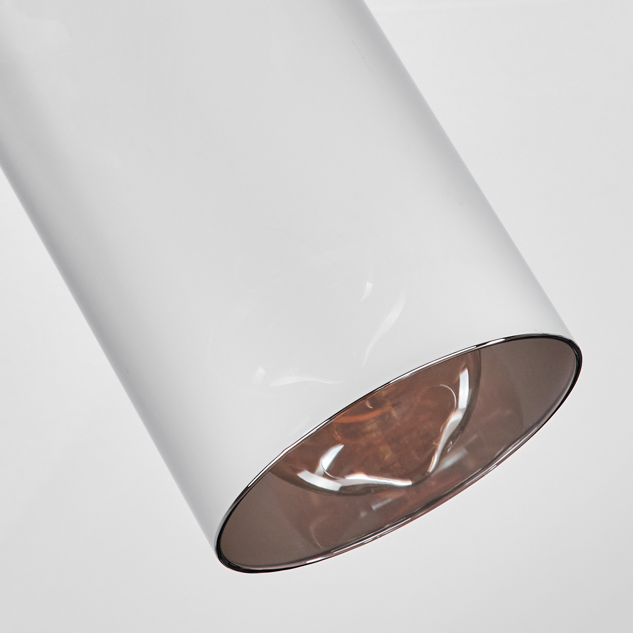 Ein weißes, zylindrisches Objekt, möglicherweise eine Leuchte, diagonal angewinkelt. Der Boden hat ein bronzefarbenes Innenteil mit Silberrand.