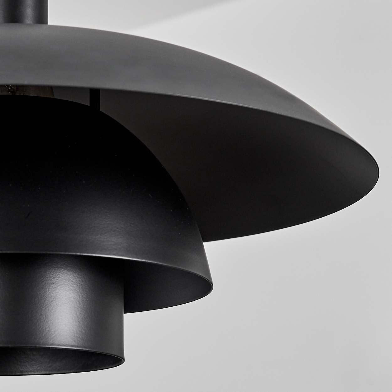 Nahaufnahme einer schwarzen, geschichteten Lampe vor weißem Hintergrund. Die Lampe hat ein abgerundetes, gestuftes Design.
