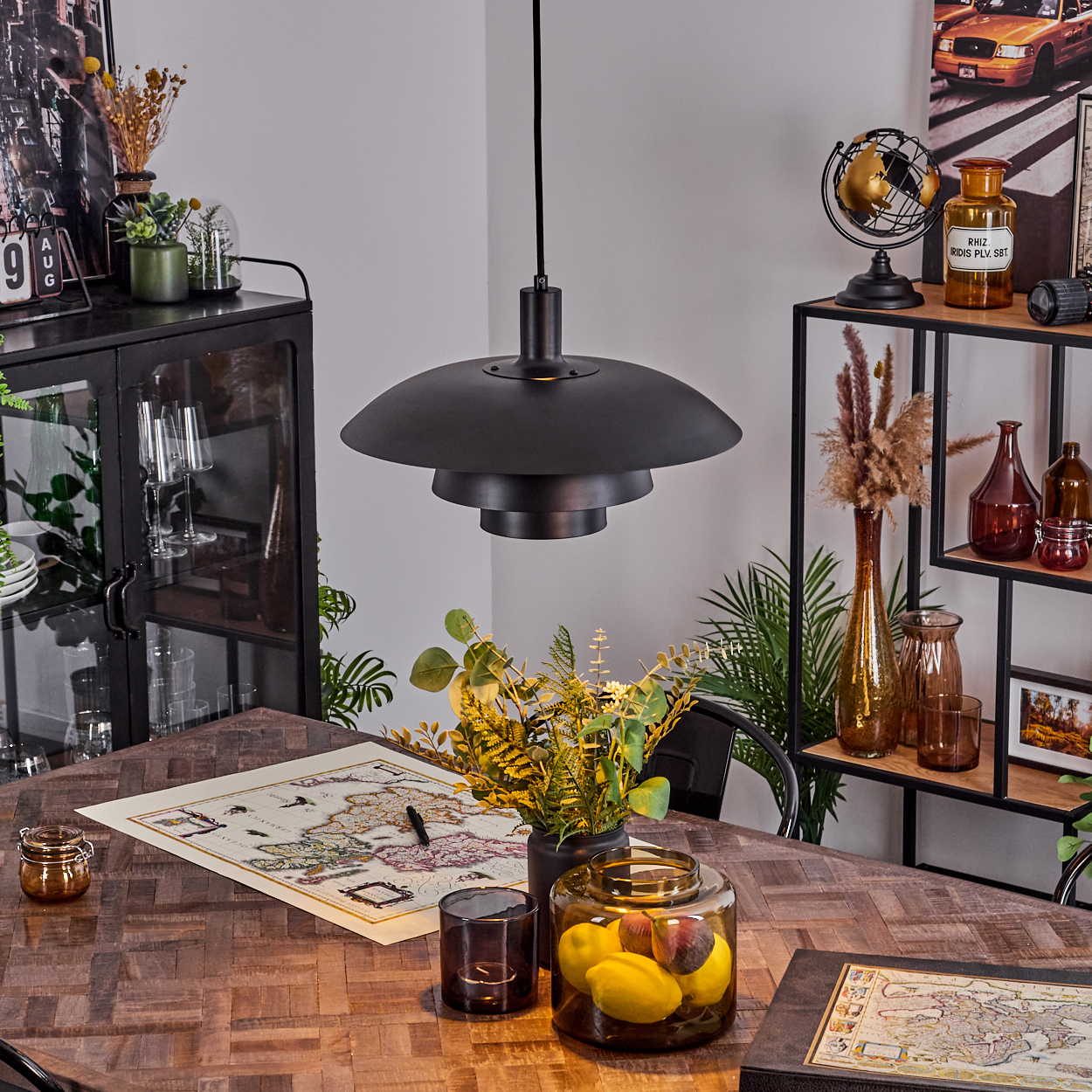 Esszimmer mit Holztisch, schwarzer Lampe und Dekorationsgegenständen wie Karte, Vasen und Glasgefäß mit Zitronen.
