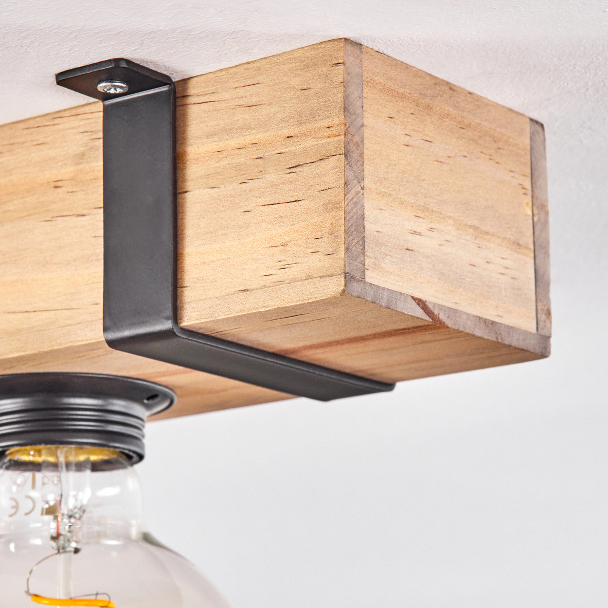 Deckenleuchte mit Holzbalken. Unter dem Holzblock ist eine Glühbirne zu sehen, die von einer schwarzen Metallhalterung getragen wird.