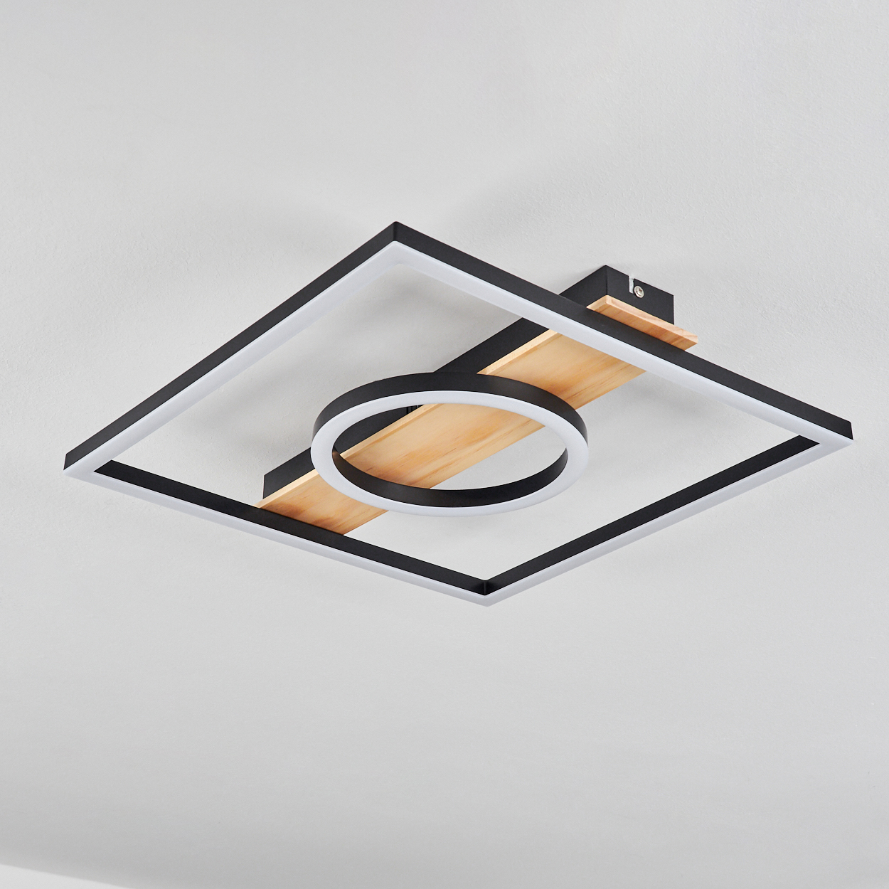 Eine moderne Deckenleuchte. Sie hat einen quadratischen Rahmen mit einem kreisförmigen Licht in der Mitte. Holzbalken und weiße Decke im Hintergrund.