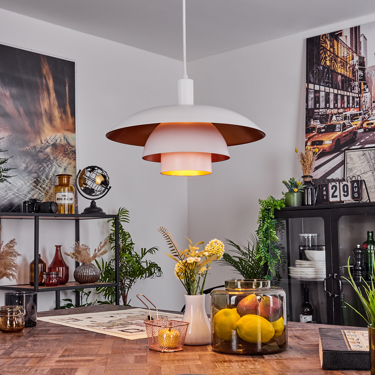 Ein Raum mit einer weißen und goldenen Lampe, einem Holztisch, Pflanzen und einem Glasbehälter mit Zitronen. Ein Gemälde hängt an der Wand.