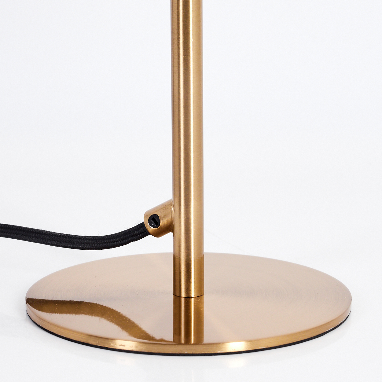 Ein goldfarbener Lampensockel mit schwarzem Kabel auf weißem Hintergrund. Der Sockel ist kreisförmig und die Lampenstange zylindrisch.