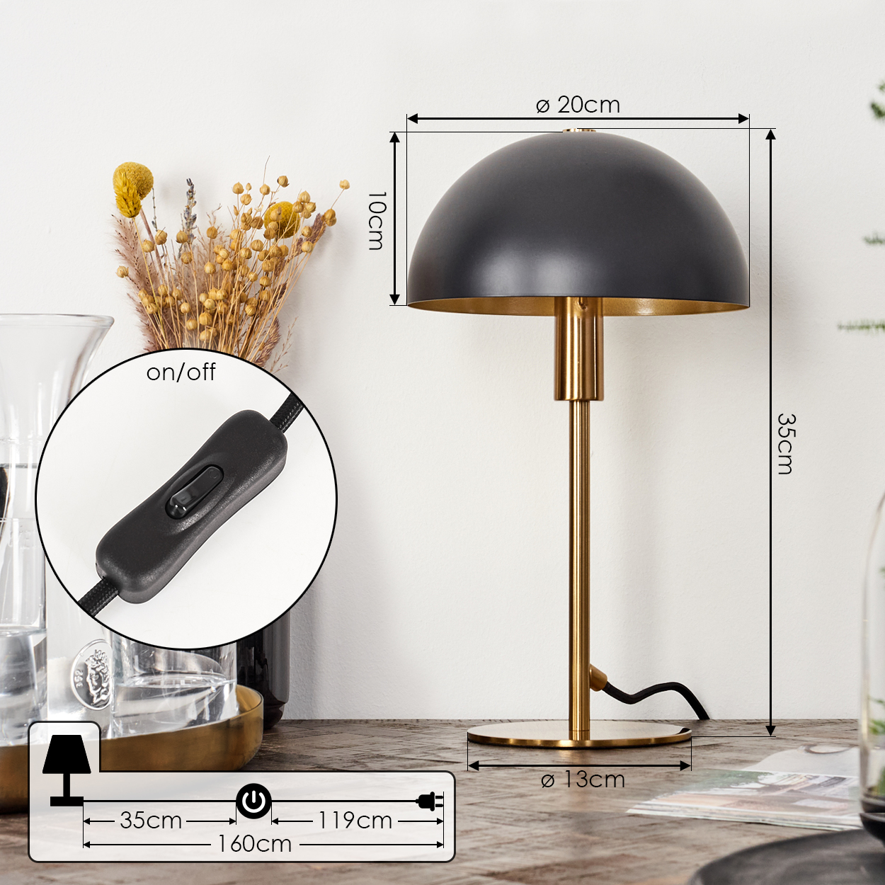 Eine schwarz-goldene Tischlampe mit Maßen. Ein Schalter ist mit der Aufschrift Ein/Aus zu sehen. Getrocknete Blumen und andere Gegenstände sind im Hintergrund.