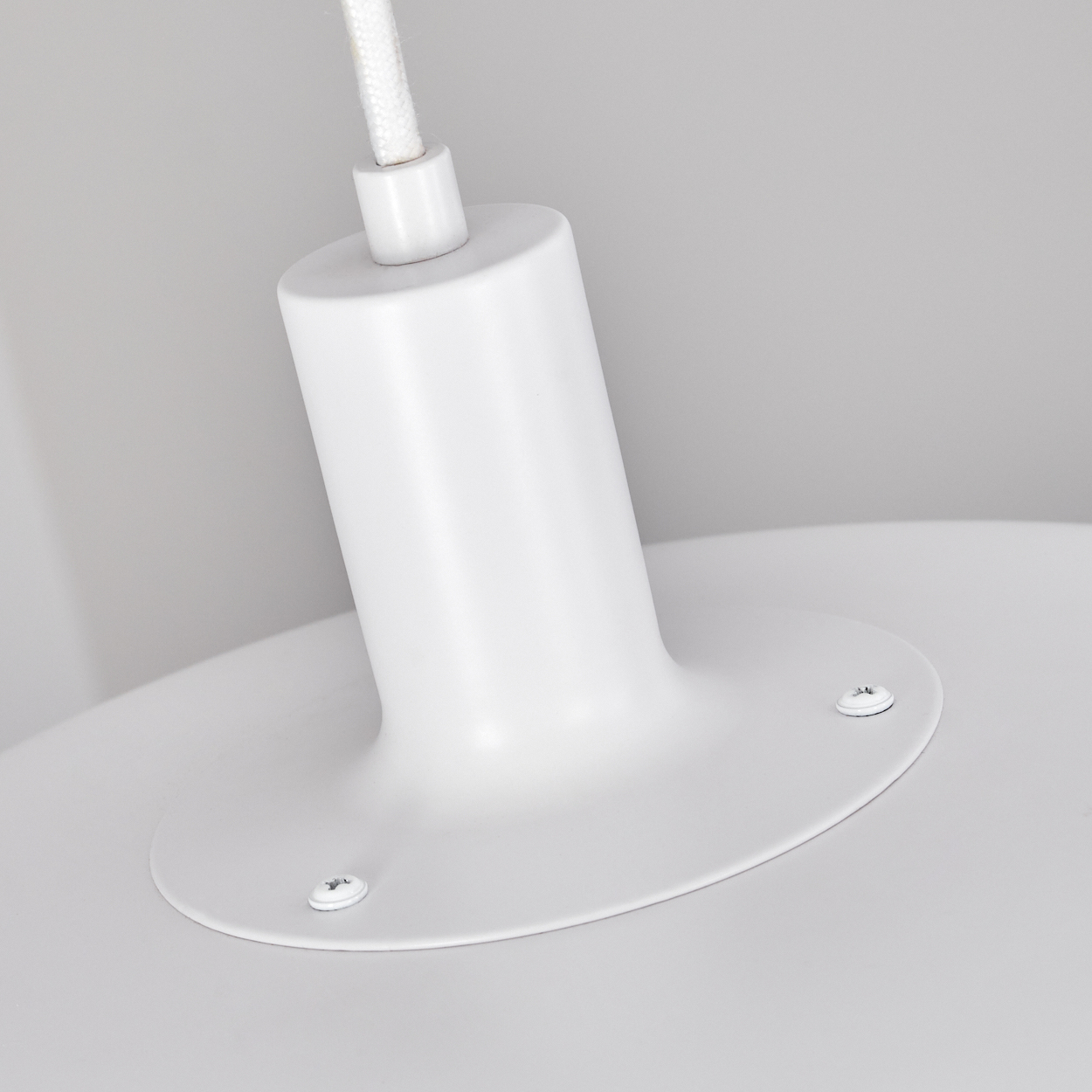 Nahaufnahme einer weißen Deckenlampe. Die Lampe hat einen weißen zylindrischen Sockel, eine runde Platte und ein weißes Kabel.