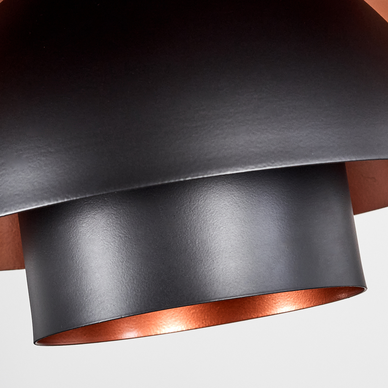Nahaufnahme eines schwarzen Metalllampenschirms mit kupferfarbenem Innenraum. Die Lampe hat ein mehrschichtiges Design. Weißer Hintergrund.
