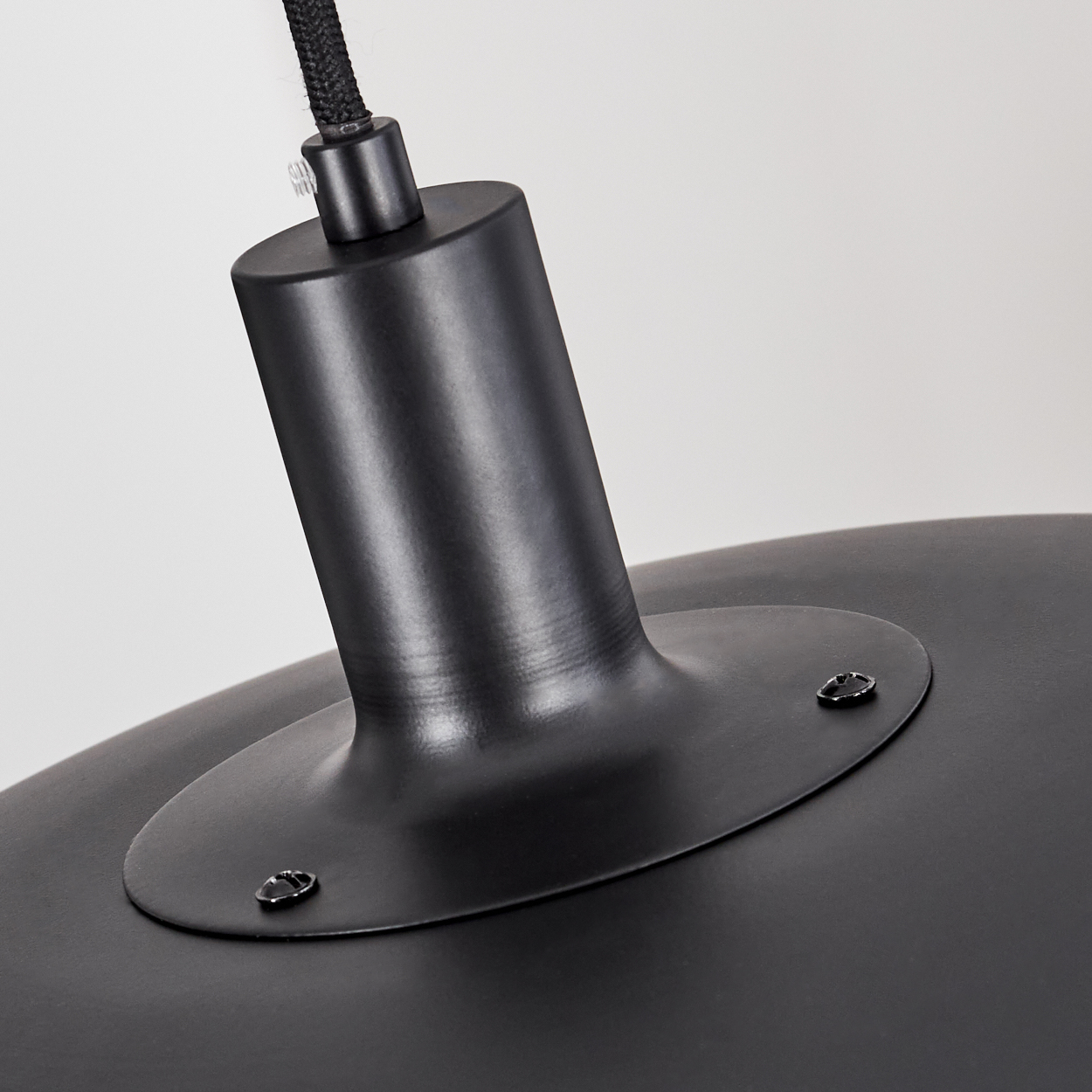 Nahaufnahme einer schwarzen, modernen Lampe. Sie hat einen runden Schirm und einen zylindrischen Stiel mit schwarzem Kabel. Der Hintergrund ist weiß.
