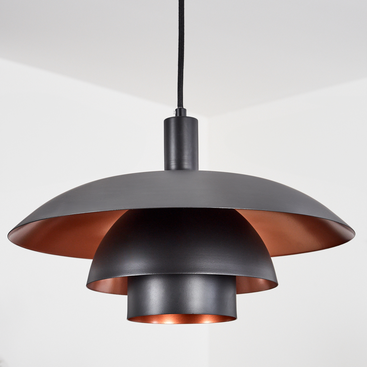 Eine moderne Pendelleuchte mit mehrschichtigem Design. Die Lampe hat ein dunkelgraues Äußeres und ein kupferfarbenes Inneres, das an einem schwarzen Kabel hängt.