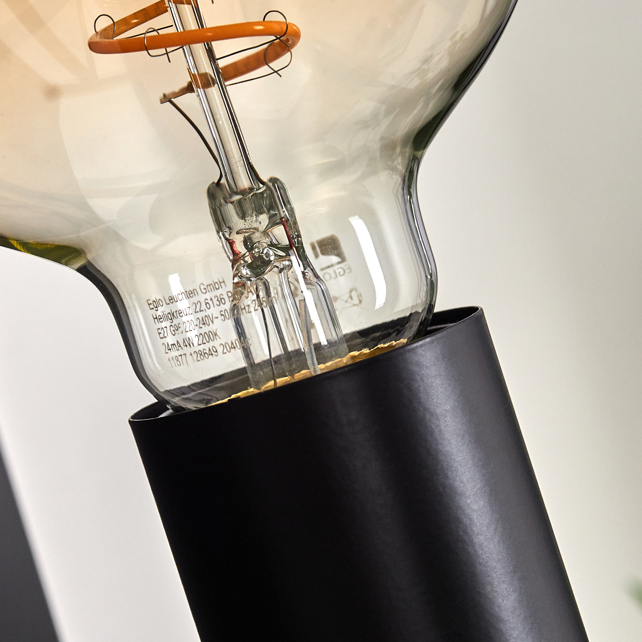 Nahaufnahme einer Edison-Glühbirne. Die Birne hat einen schwarzen Sockel und klares Glas mit gelbem Glühfaden. Text ist auf dem Glas sichtbar.