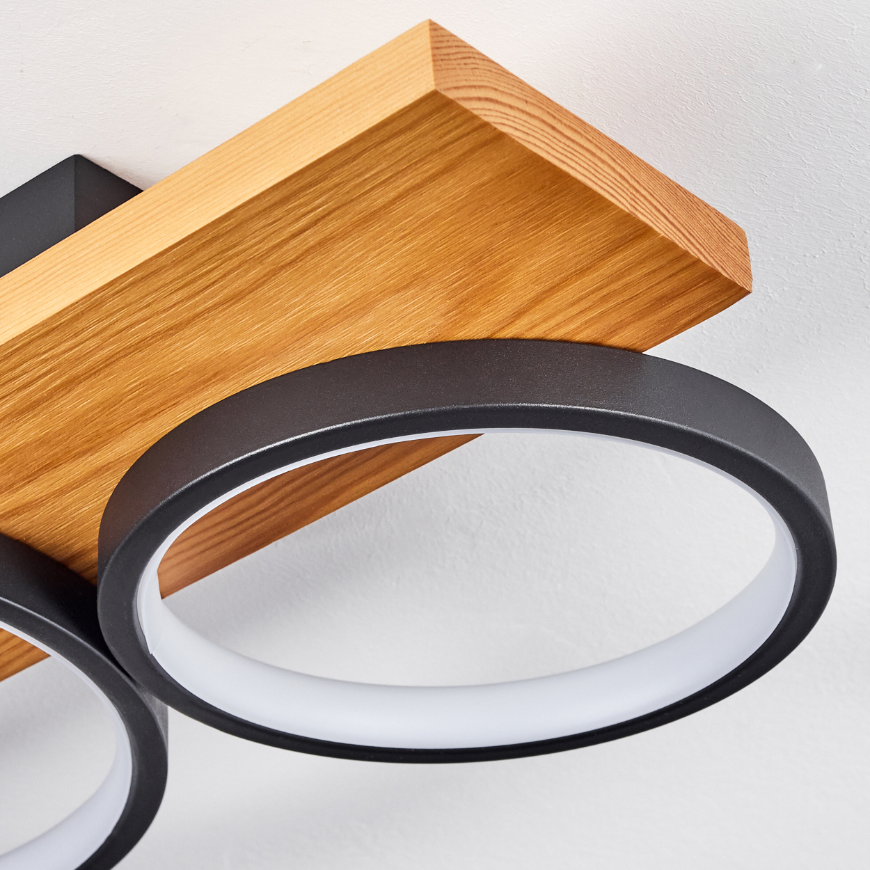 Eine moderne Deckenleuchte mit einem Holzblock und zwei schwarzen kreisförmigen Leuchten mit weißen Innenringen.