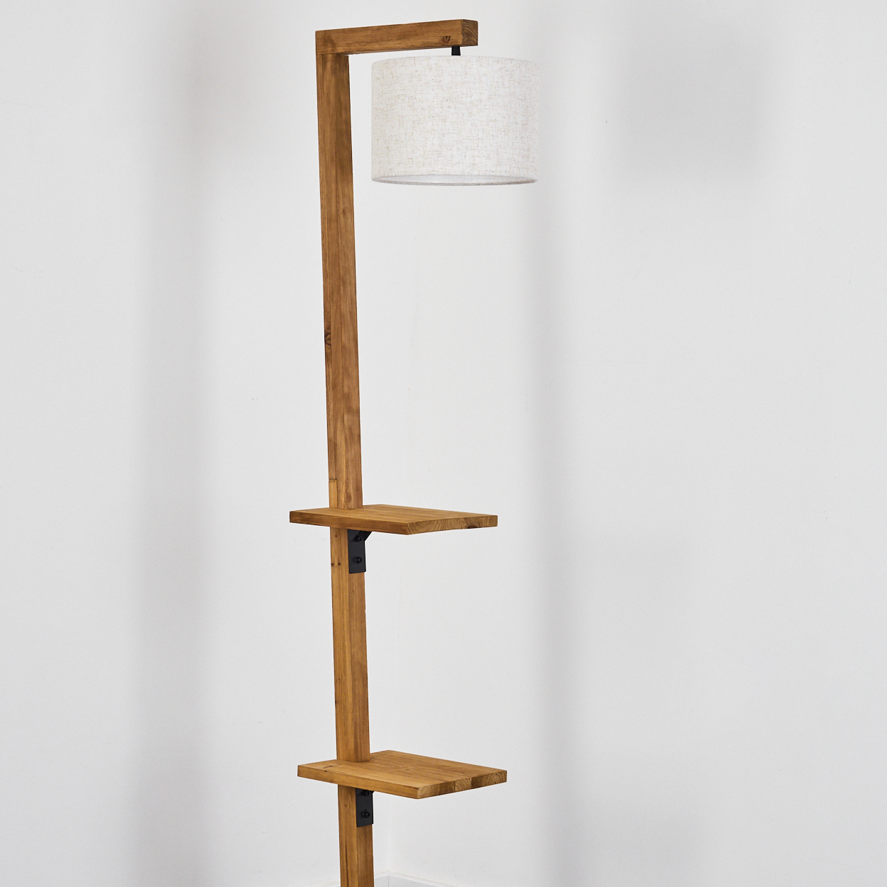 Eine Stehlampe aus Holz mit zwei Ablagen, einem Lampenschirm und einem rechteckigen Rahmen. Der Hintergrund ist eine weiße Wand.