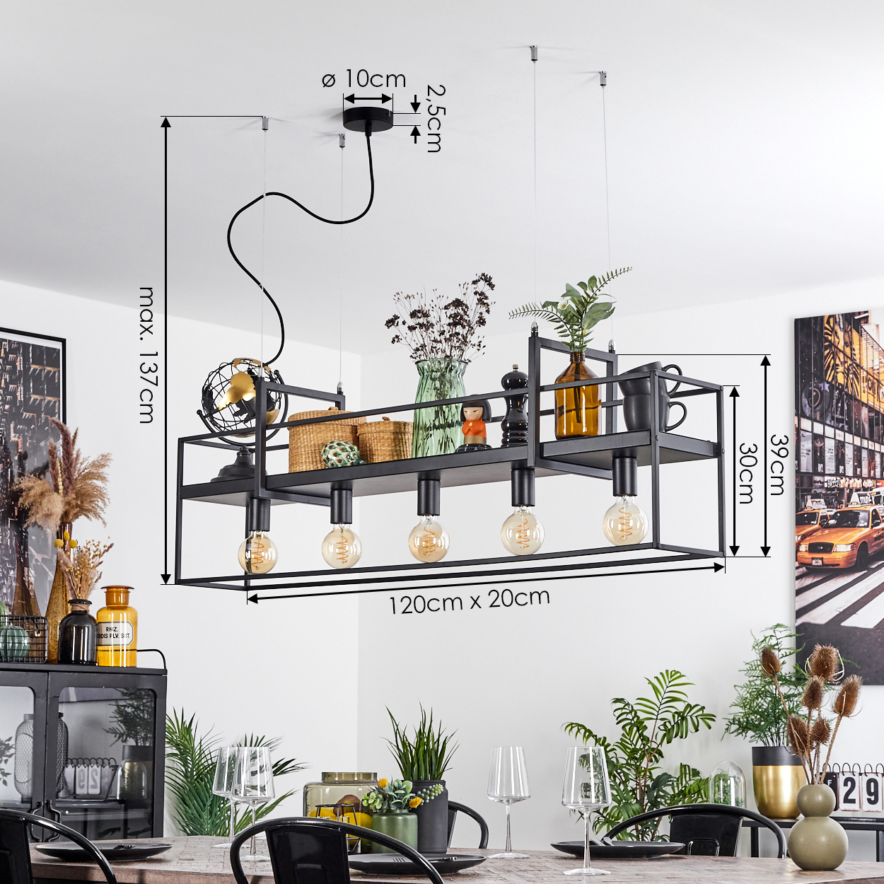 Eine schwarze, rechteckige Pendelleuchte mit Edison-Glühbirnen hängt über einem Esstisch mit Pflanzen, Gläsern und einem Gemälde im Hintergrund.