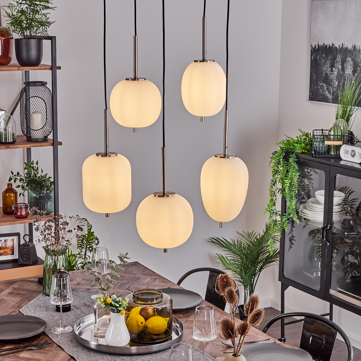 Esszimmer. Fünf Pendelleuchten hängen über einem Tisch, der für das Abendessen gedeckt ist. Pflanzen und Dekoration befinden sich im Hintergrund.
