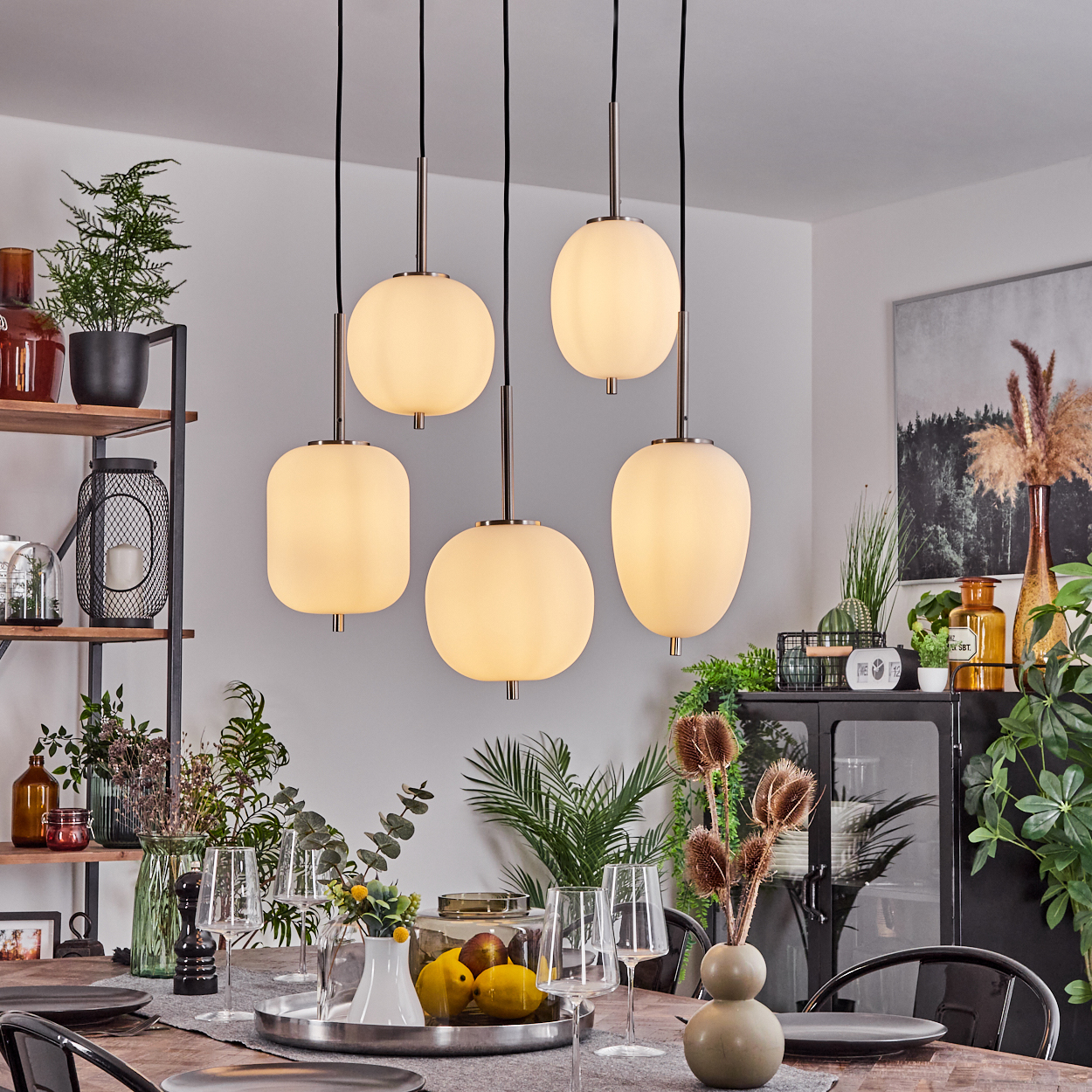 Ein Esszimmer mit Holztisch, Stühlen und fünf Hängelampen. Der Tisch ist mit Gläsern, Tellern und dekorativen Gegenständen gedeckt.
