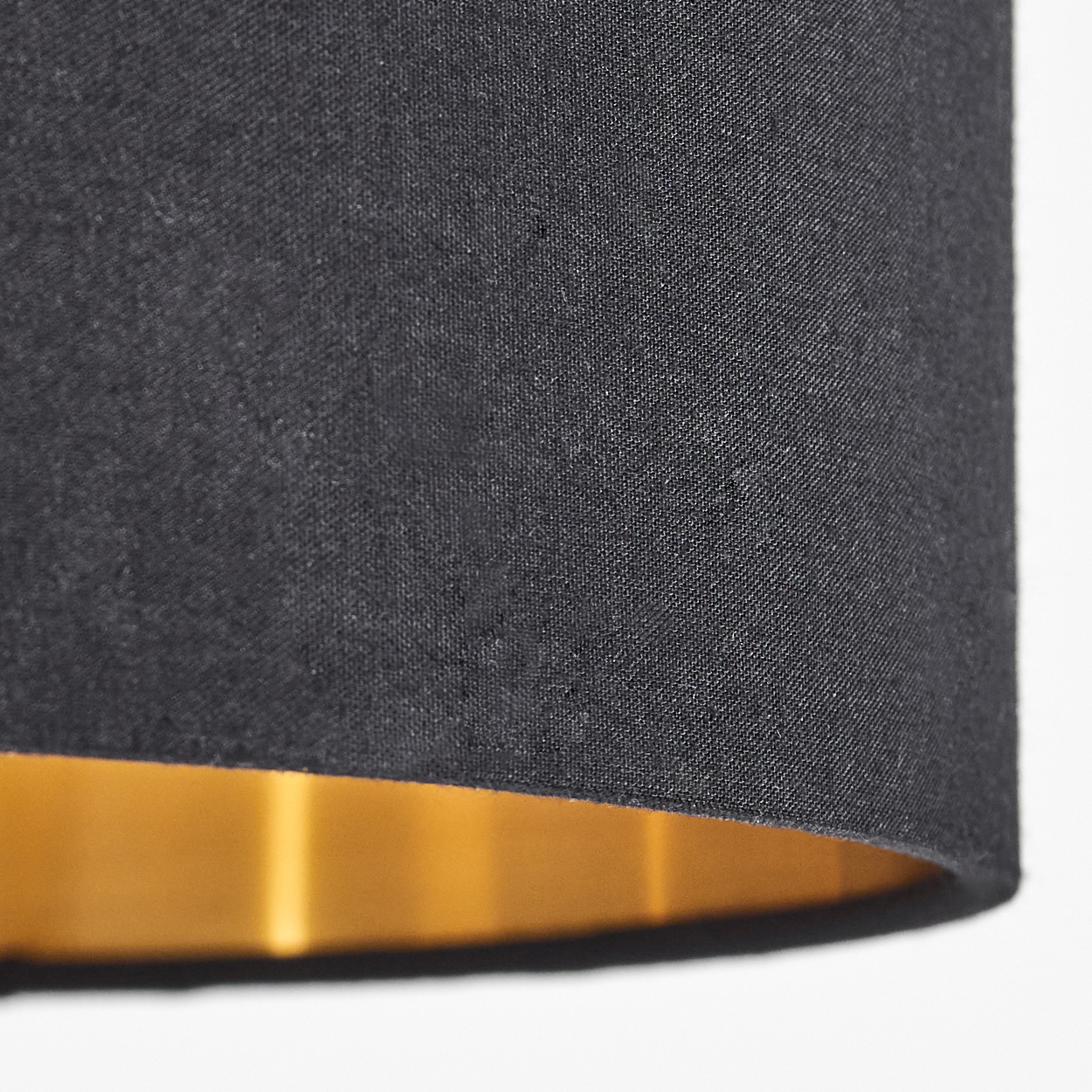 Nahaufnahme eines schwarzen Lampenschirms. Die Innenseite ist golden. Der Hintergrund ist weiß.