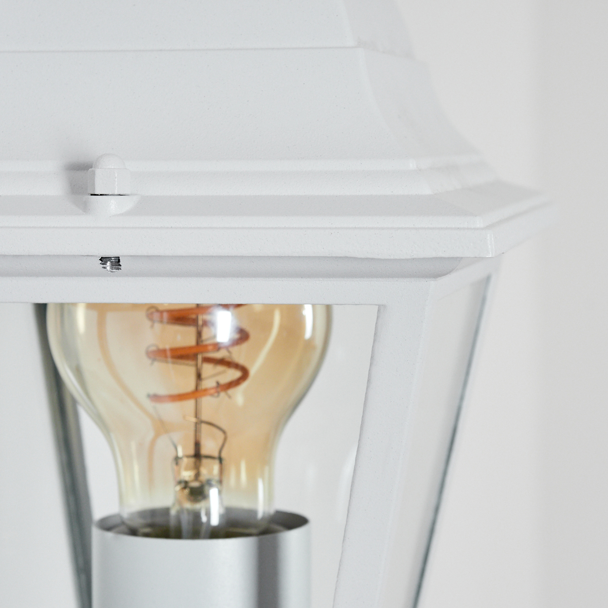 Nahaufnahme einer weißen Außenlampe mit sichtbarer Glühbirne. Die Birne hat einen Wendel, vor weißem Hintergrund.