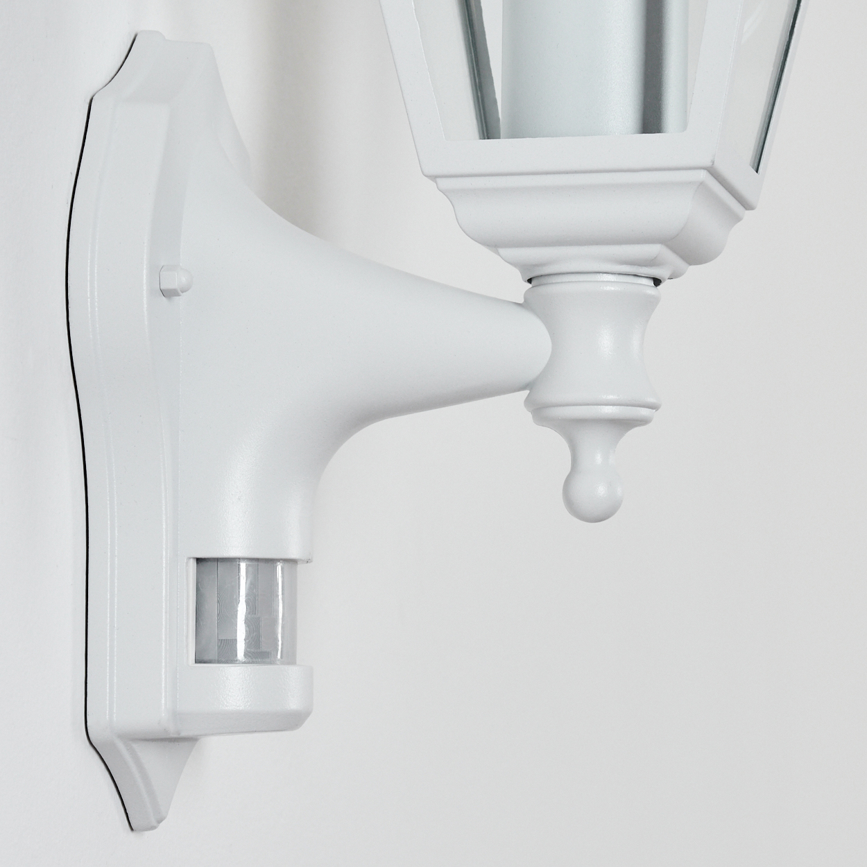 Weiße Wandlampe mit Bewegungssensor. Die Lampe hat ein klassisches Design mit laternenförmigem Schirm. Sie ist an einer weißen Wand befestigt.