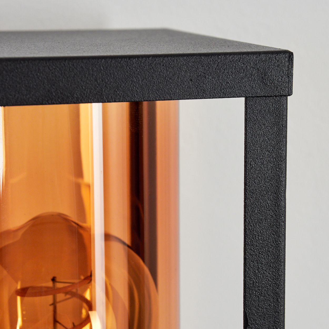 Nahaufnahme eines schwarzen Metalllampengestells. Im Inneren befindet sich ein orangefarbener Glaszylinder mit einer Glühbirne.