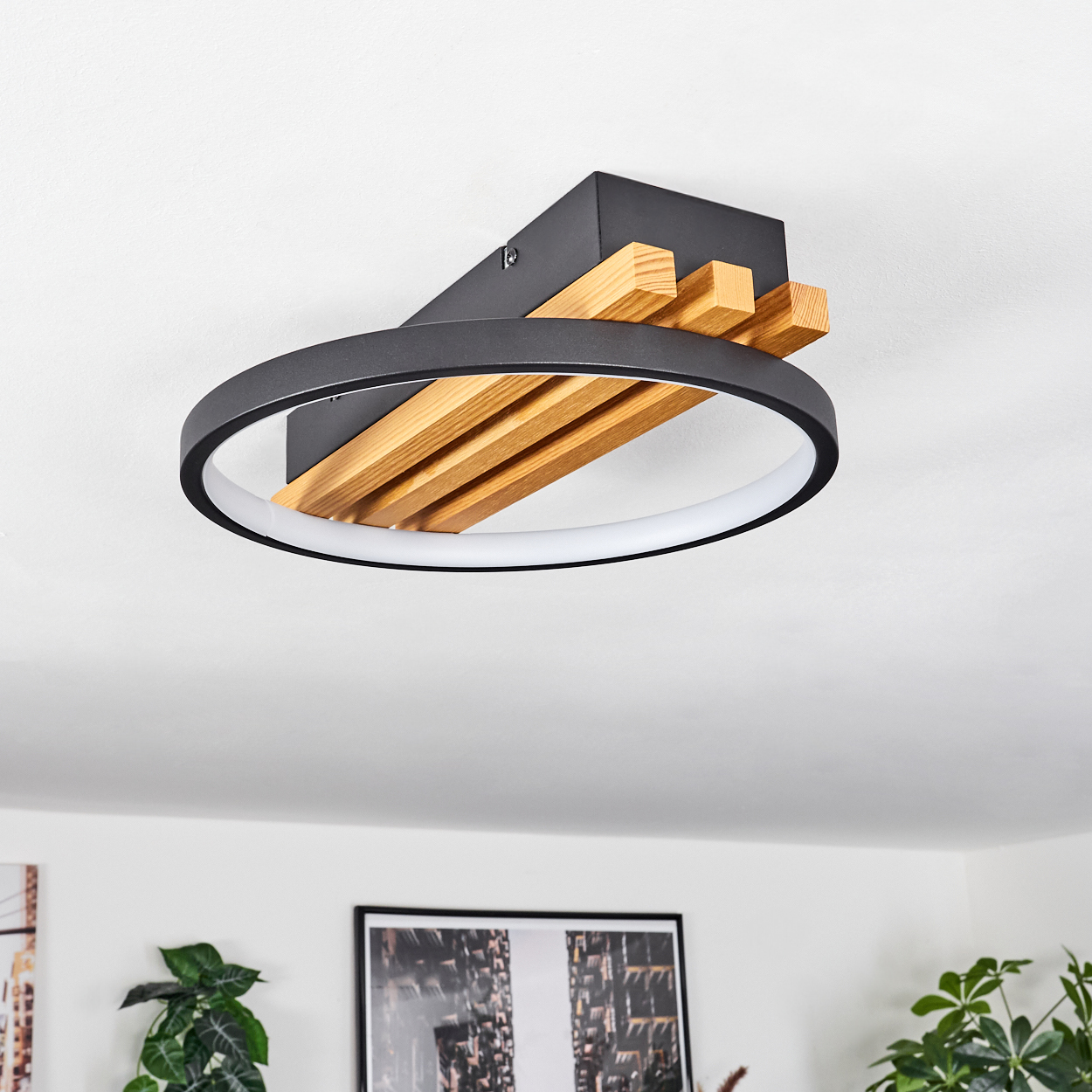 Eine moderne Deckenleuchte mit schwarzem Rahmen, Holzlatten und einem weißen Leuchtring, montiert an einer weißen Decke.