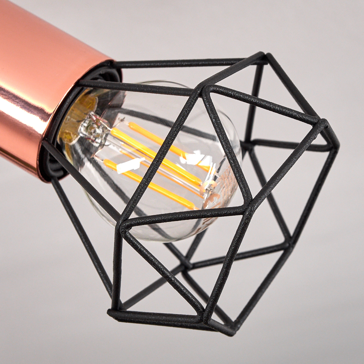 Eine moderne Leuchte mit kupferfarbenem zylindrischen Sockel und einem schwarzen geometrischen Käfig, der eine Glühbirne umschließt.