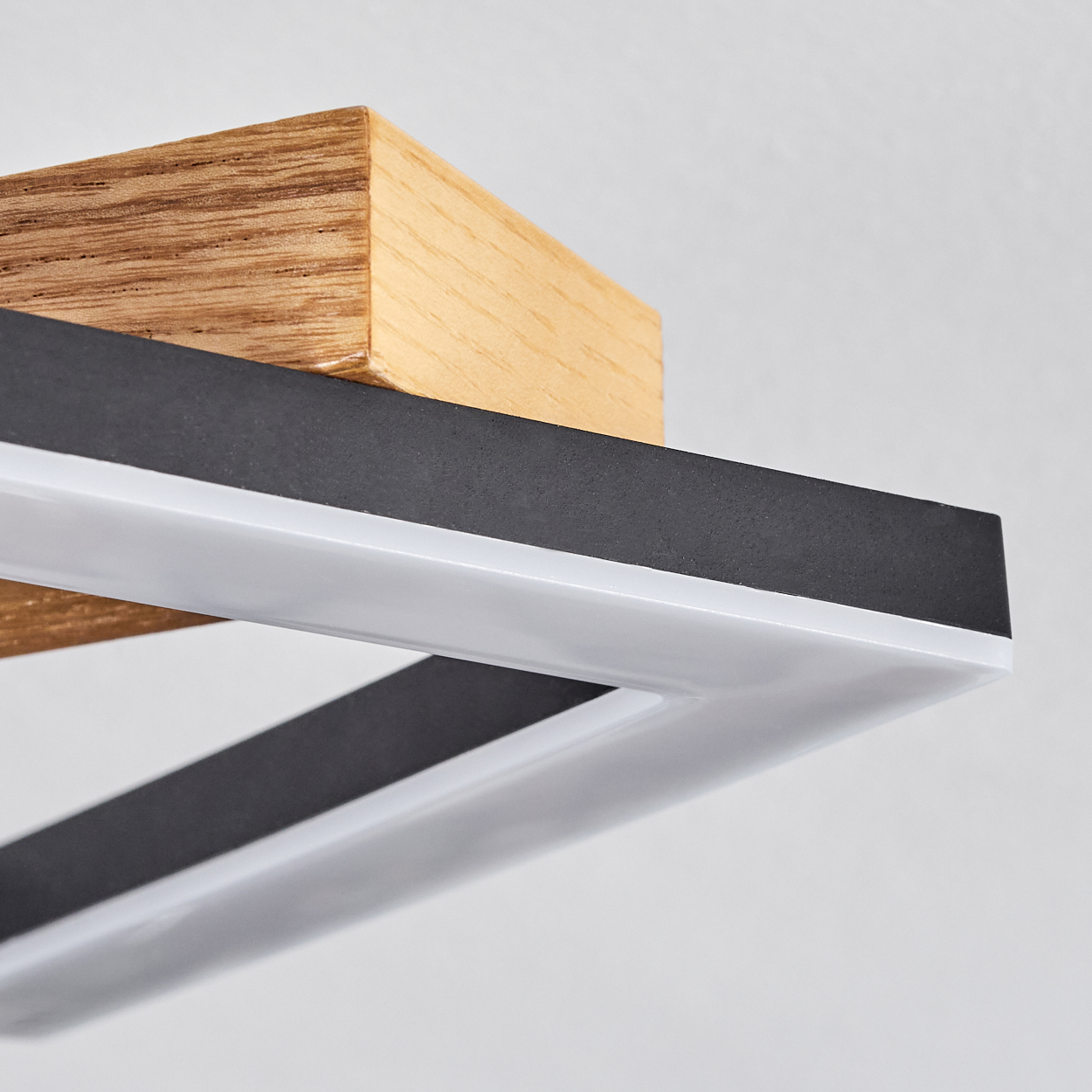 Nahaufnahme einer modernen Lampe. Sie hat einen Holzblock, einen schwarzen Rahmen und einen weißen Lichtstreifen. Der Hintergrund ist weiß.