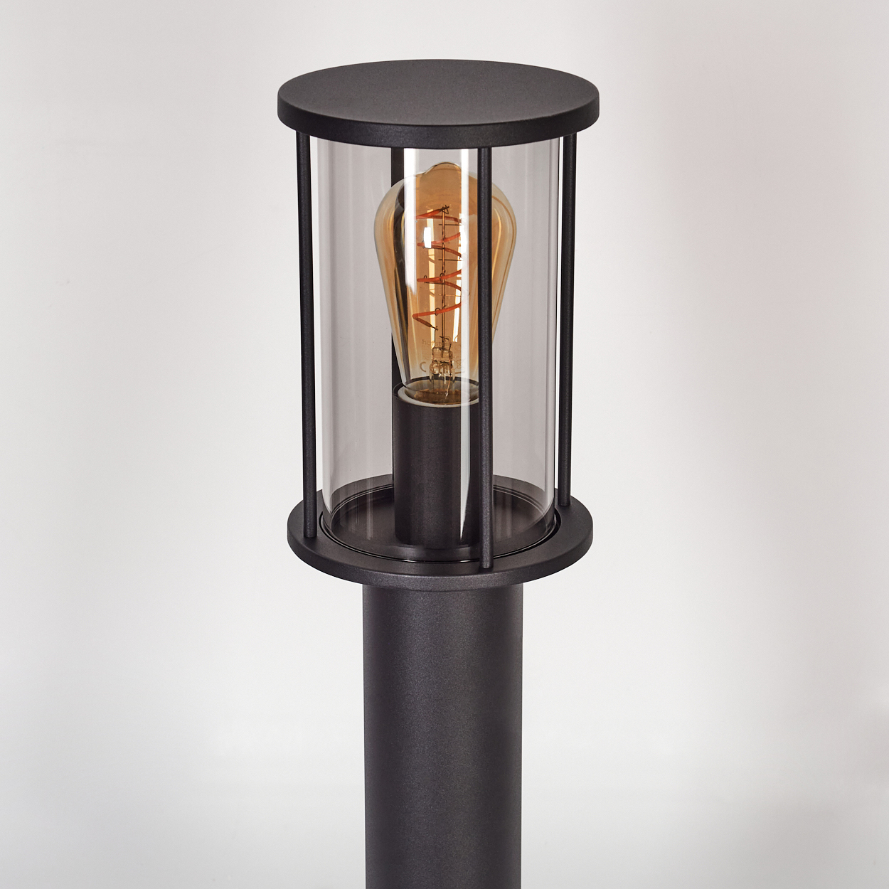 Eine schwarze Außenlampe mit Glasgehäuse und Glühbirne. Sie befindet sich auf weißem Hintergrund.