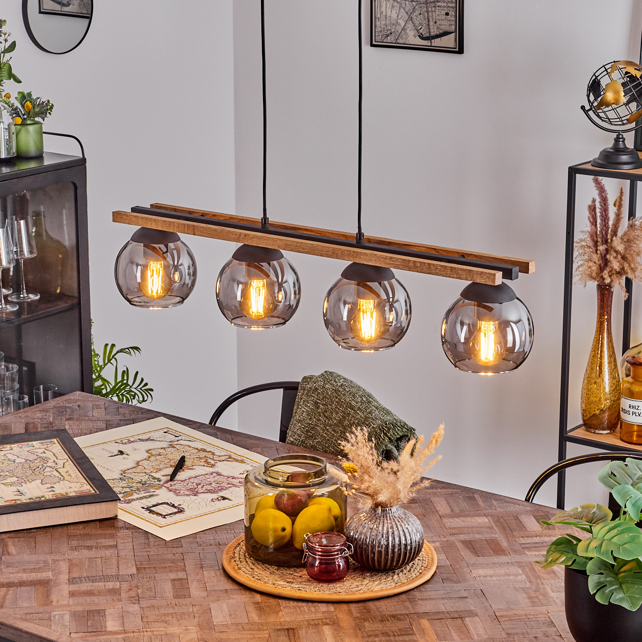 Esszimmer mit Holztisch, Hängeleuchte und Dekorationsgegenständen. Auf dem Tisch liegen eine Karte und ein Glas mit Obst.