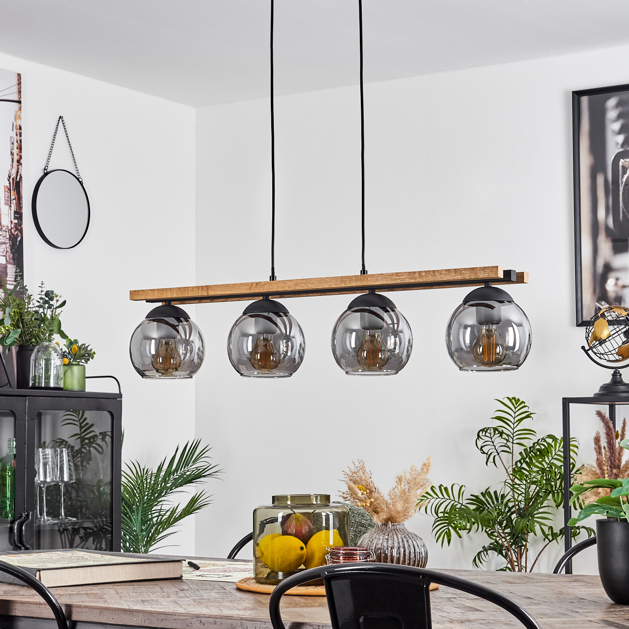 Esszimmer mit Holztisch, Hängelampen und Dekorationsartikeln. Ein schwarz gerahmter Spiegel hängt an der Wand.