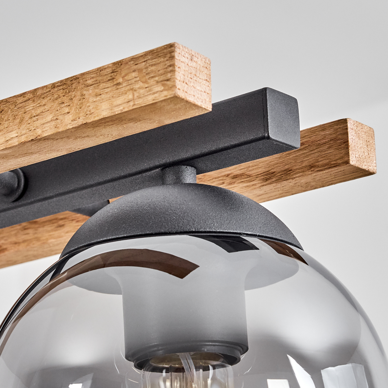 Nahaufnahme einer modernen Lampe. Sie hat einen Glasschirm, einen Holzbalken und eine schwarze Metallstruktur. Der Hintergrund ist weiß.