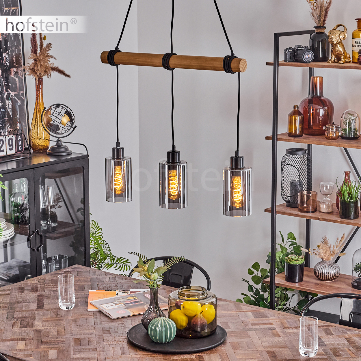 Esszimmer-Szene mit Holztisch und Pendelleuchten. Im Hintergrund ein Regal mit Dekoration.