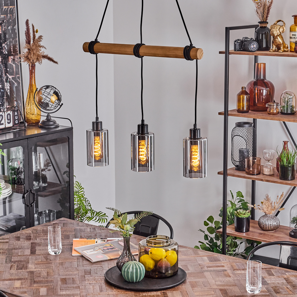 Ein Esszimmer mit Holztisch, drei Hängelampen und Dekorationsartikeln auf Regalen und dem Tisch.