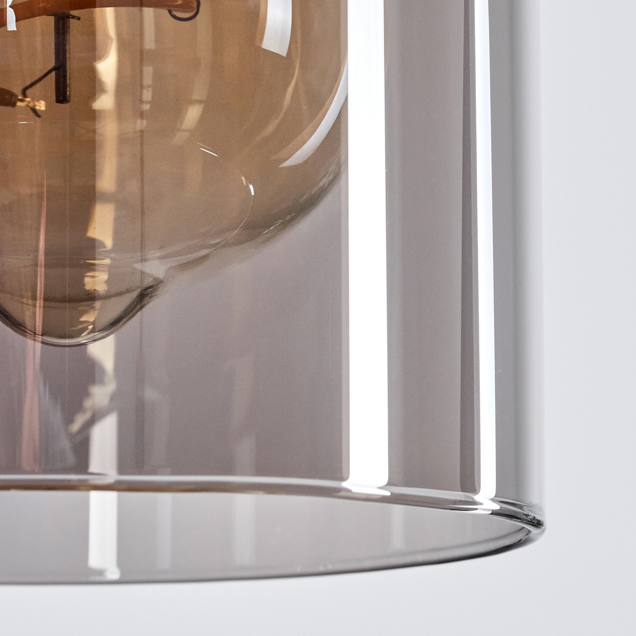 Nahaufnahme einer Glaslampe. Die Lampe hat einen zylindrischen Schirm und eine braune Glühbirne. Der Hintergrund ist weiß.