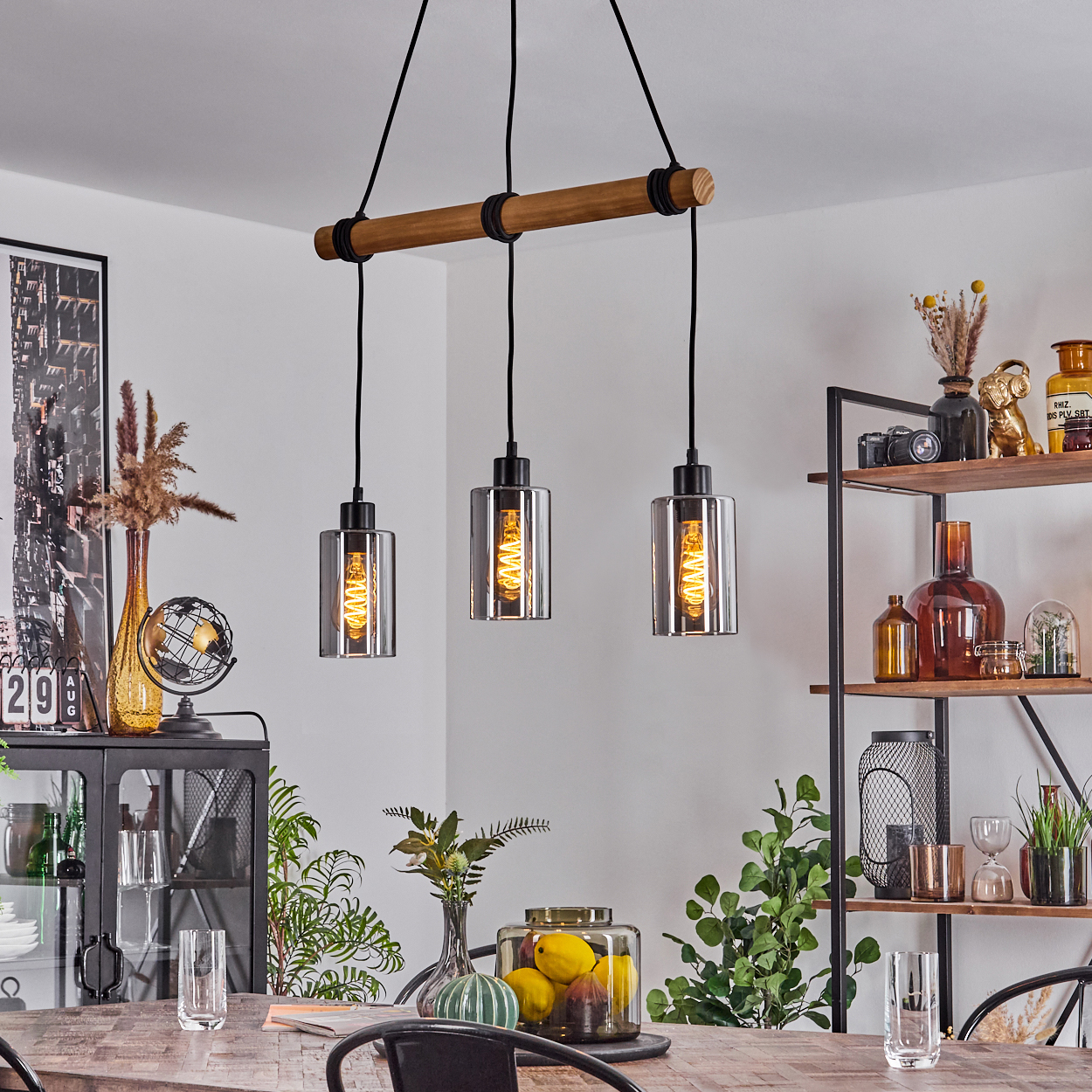 Drei Pendelleuchten hängen über einem Holztisch. Im Hintergrund steht ein Regal mit Dekoration. Weitere Dekorationen sind ebenfalls sichtbar.