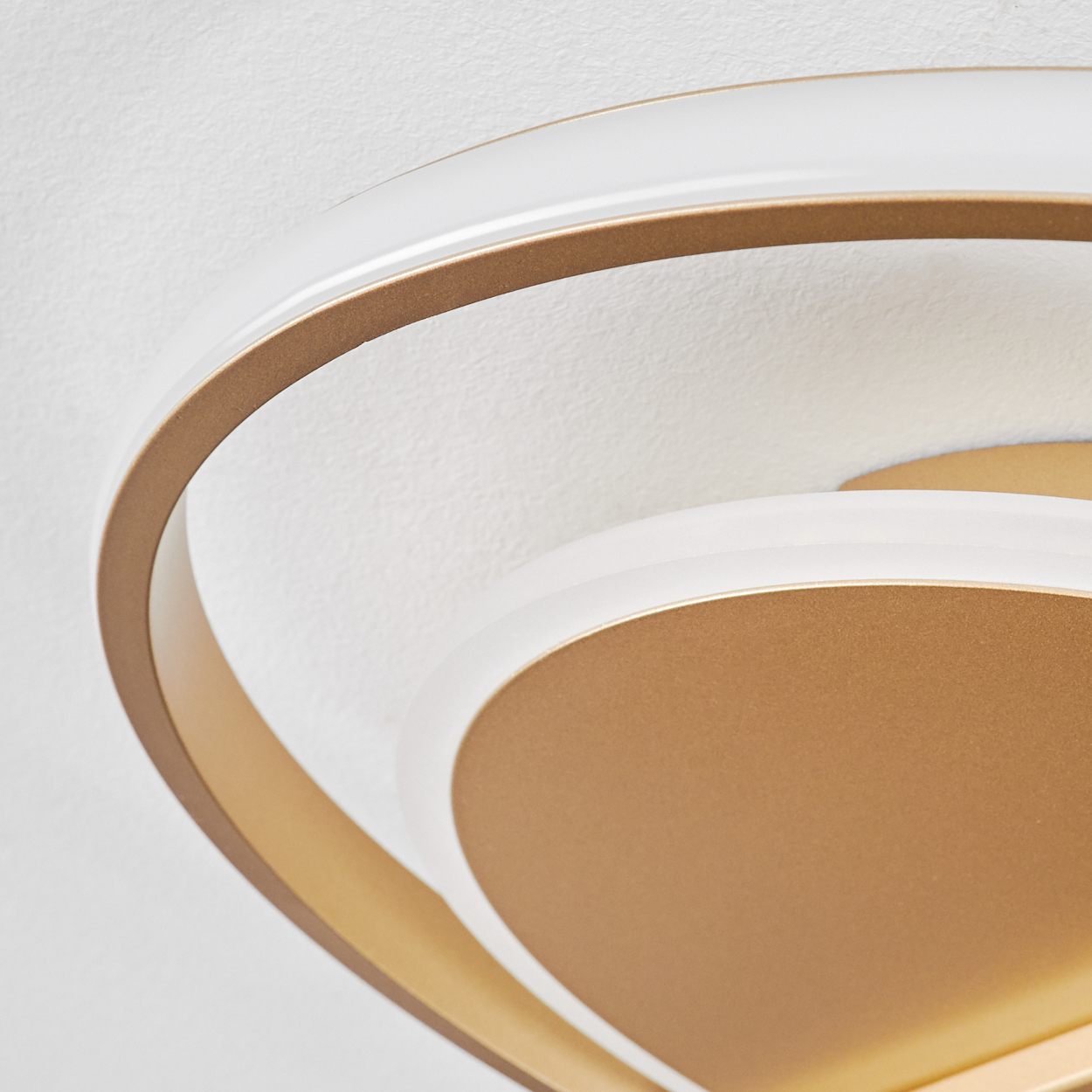 Nahaufnahme einer modernen Deckenleuchte. Sie hat goldfarbene und weiße Elemente an einer weißen Decke. Das Design ist geschwungen und geschichtet.