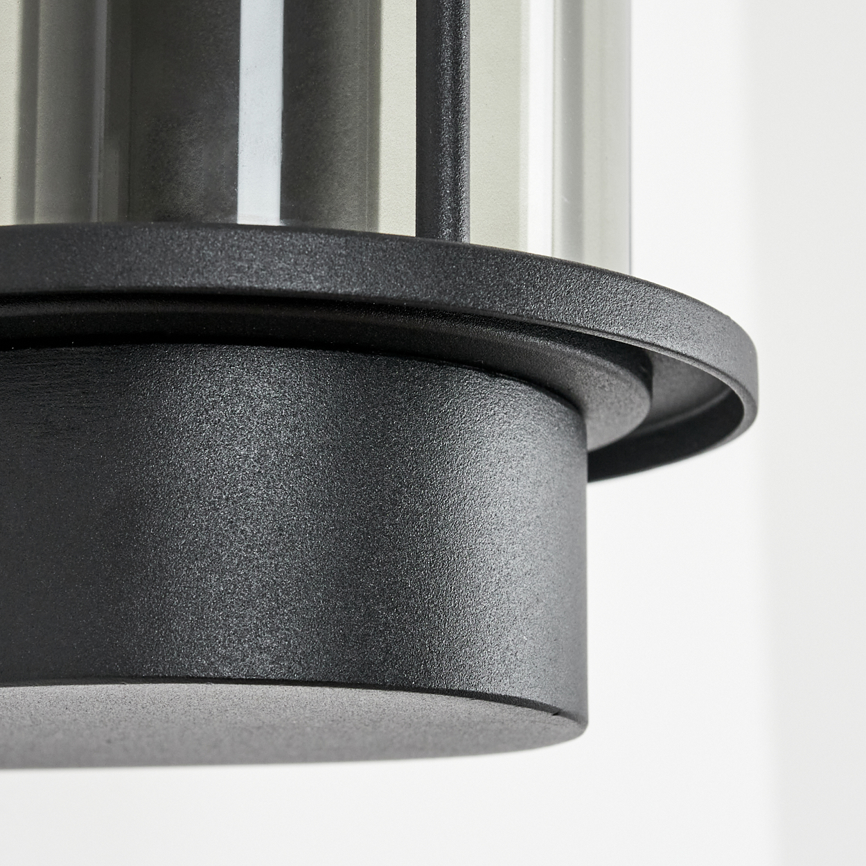 Nahaufnahme einer schwarzen Lampe mit einem durchsichtigen Glaszylinder. Die Lampe hat eine strukturierte Oberfläche und steht vor weißem Hintergrund.