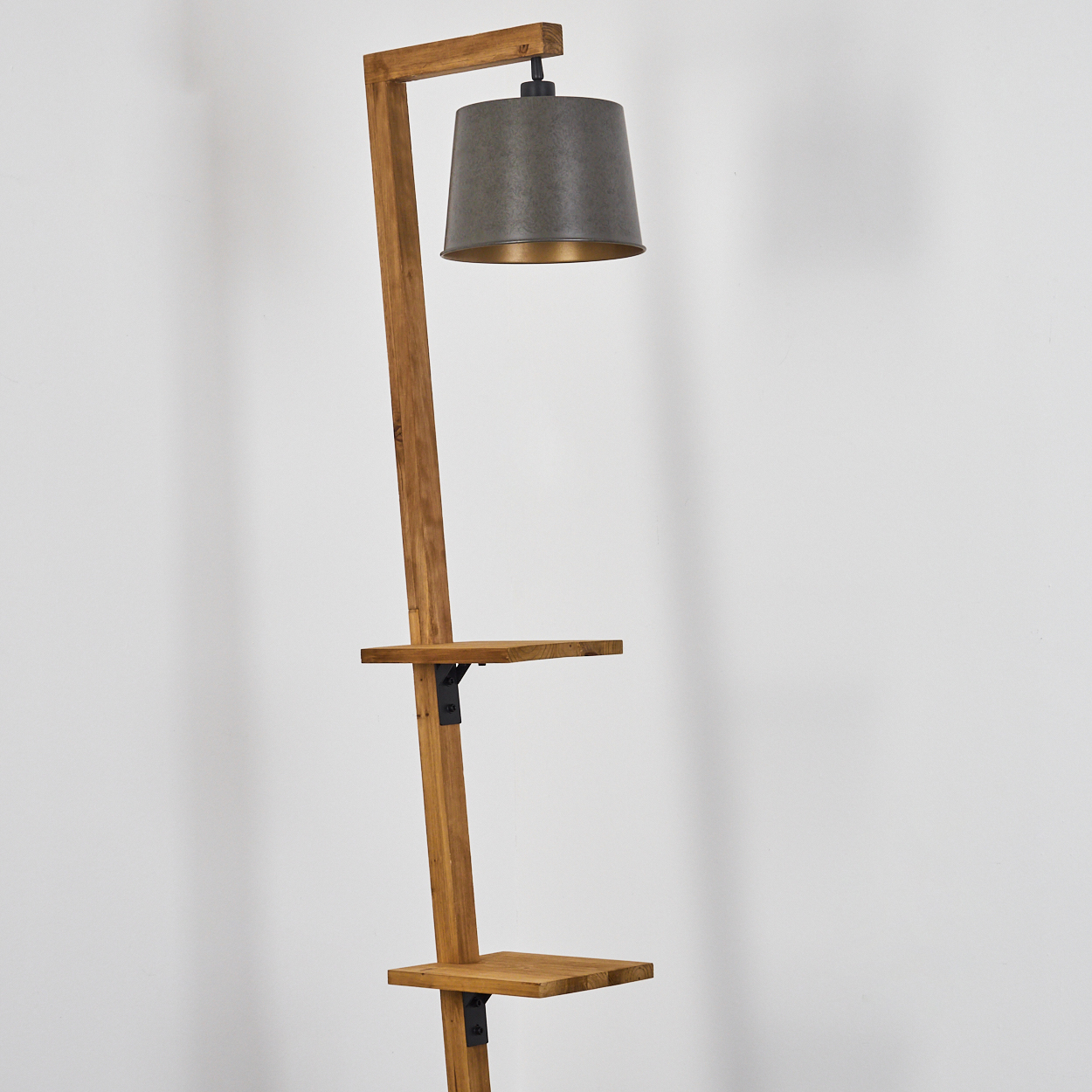 Eine Stehlampe aus Holz mit grauem Lampenschirm und zwei Regalen. Der Hintergrund ist eine weiße Wand.