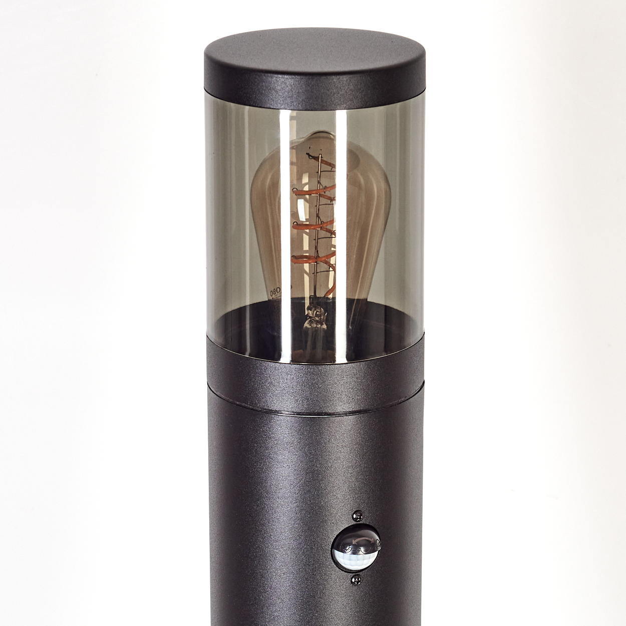 Eine schwarze zylindrische Lampe mit einer klaren, getönten Glasabdeckung, die eine dekorative Glühbirne enthüllt. Der Hintergrund ist weiß.