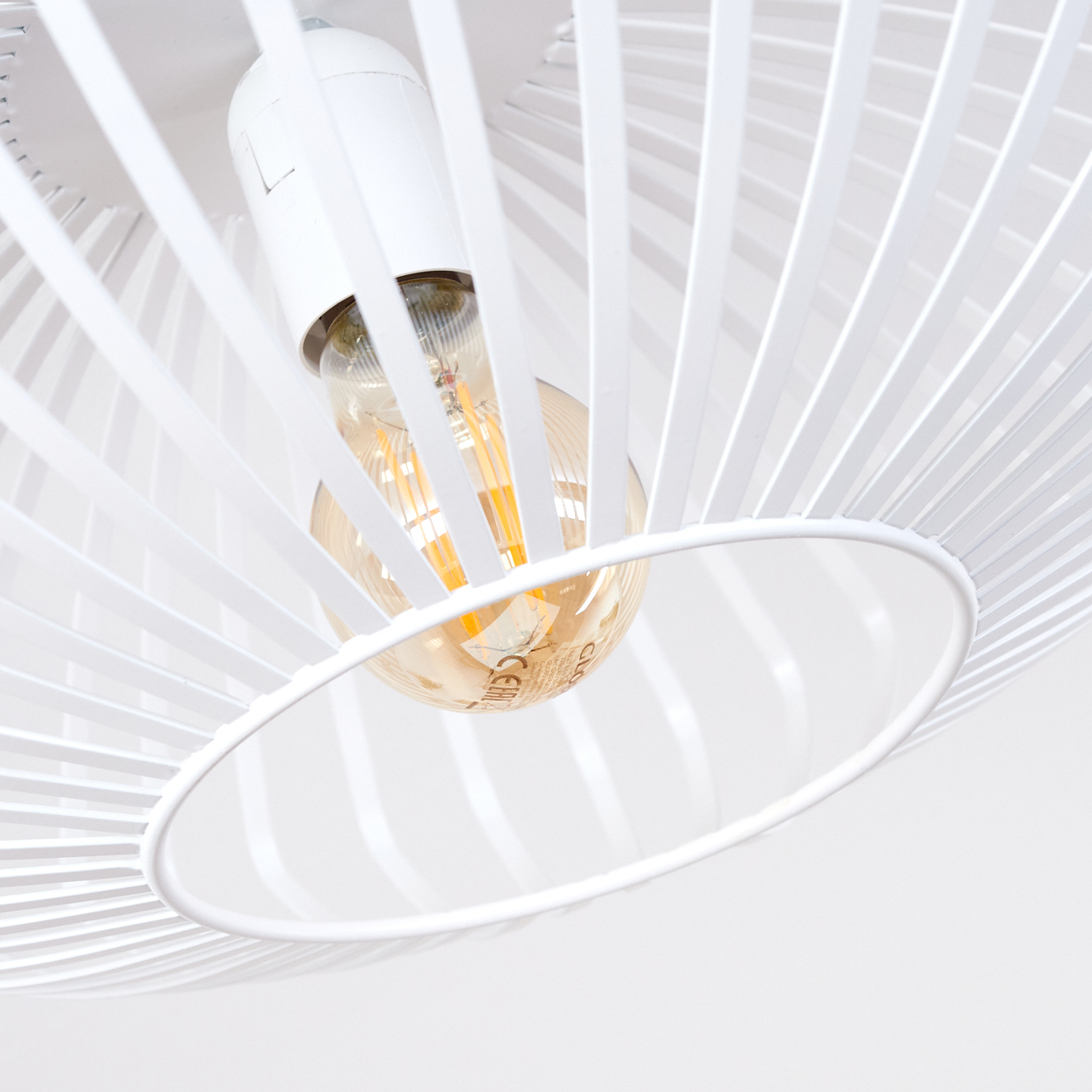 Eine weiße, moderne Deckenlampe mit sichtbarer Glühbirne. Das Design zeigt weiße Metallstäbe um die Glühbirne und eine weiße Decke.
